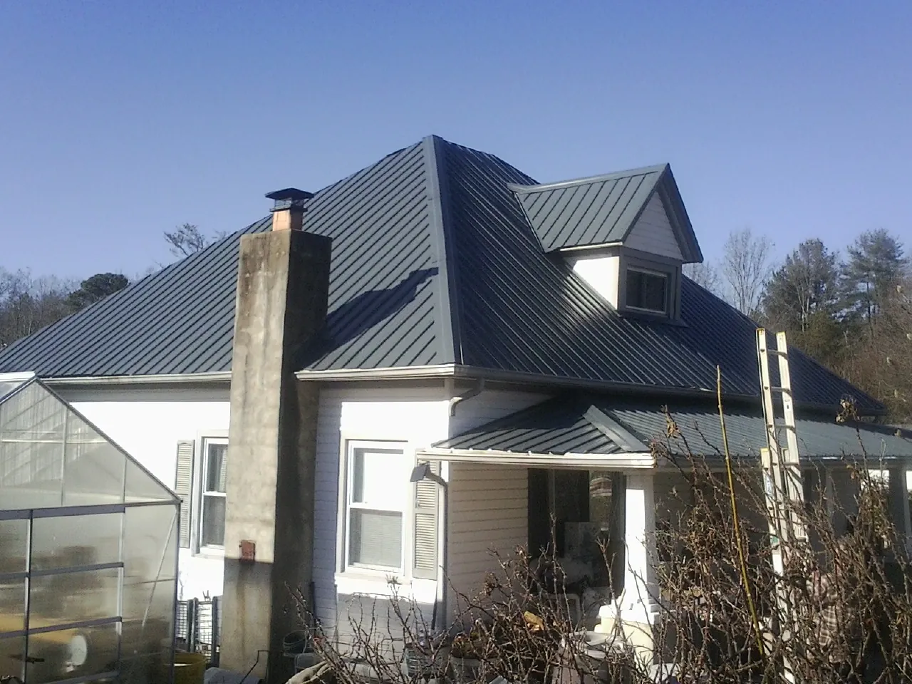 Dark blue standing seam metal roof on a white farmhouse with dormer — Slate & Tile Roof Repair by Roofing Brothers in Stewartville