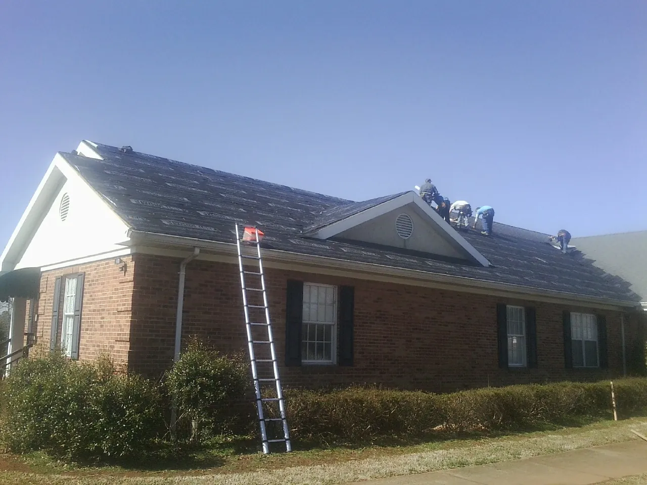 Crew tearing shingles off a brick ranch roof with a ladder set — Emergency Roof Repair work by our crew in Stewartville