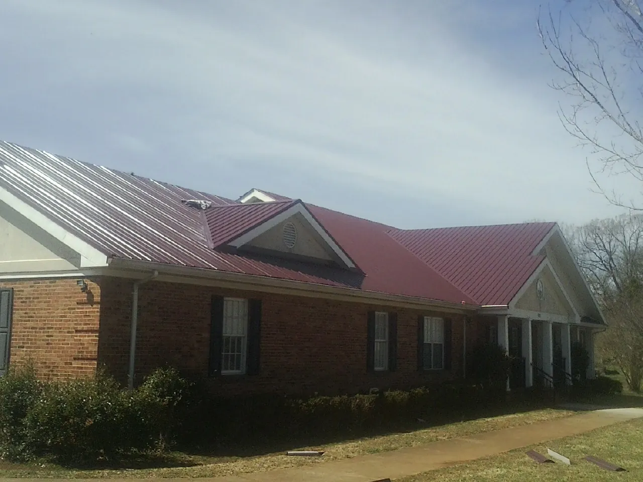 Red metal roof with gabled entries on a long brick building, from a Hail Damage Roof Repair job in Stewartville