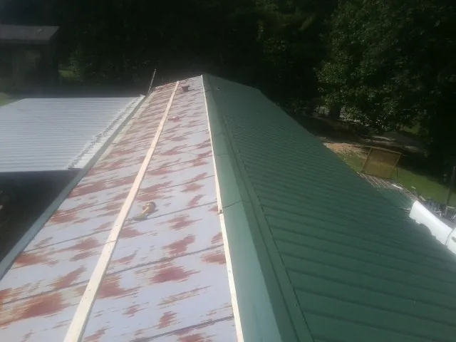 Old rusted panels beside newly installed green metal roofing — Wind Damage Roof Repair by Roofing Brothers in Stewartville
