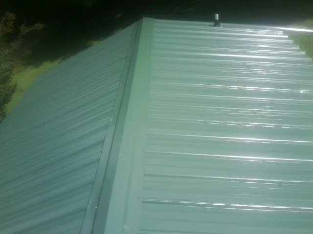New green metal panels meeting at the ridge of a roof — Flat Roof Repair work by our crew in Stewartville