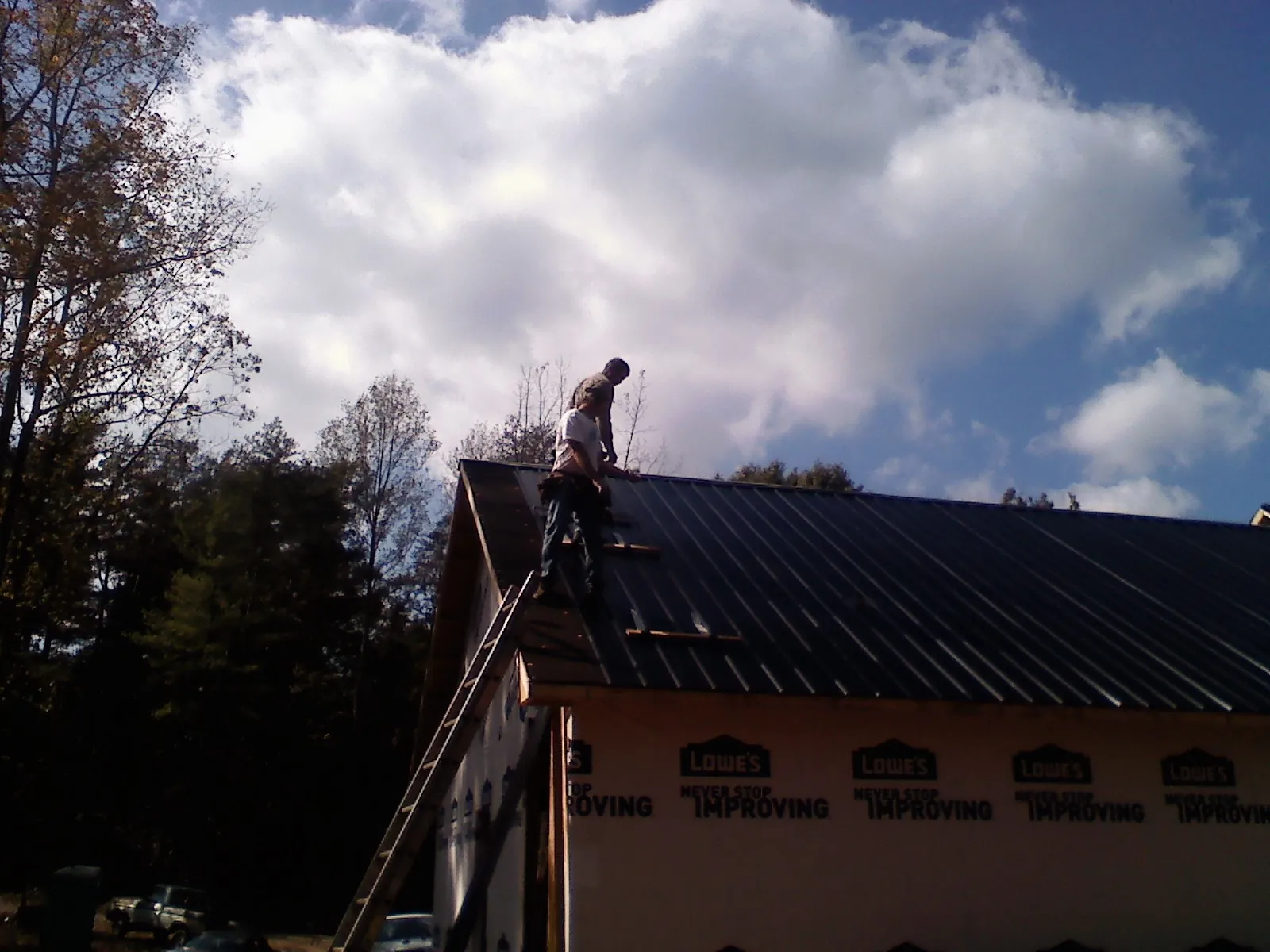 Roofer fastening dark metal panels high against a cloudy sky, from a Roof Inspection job in Stewartville