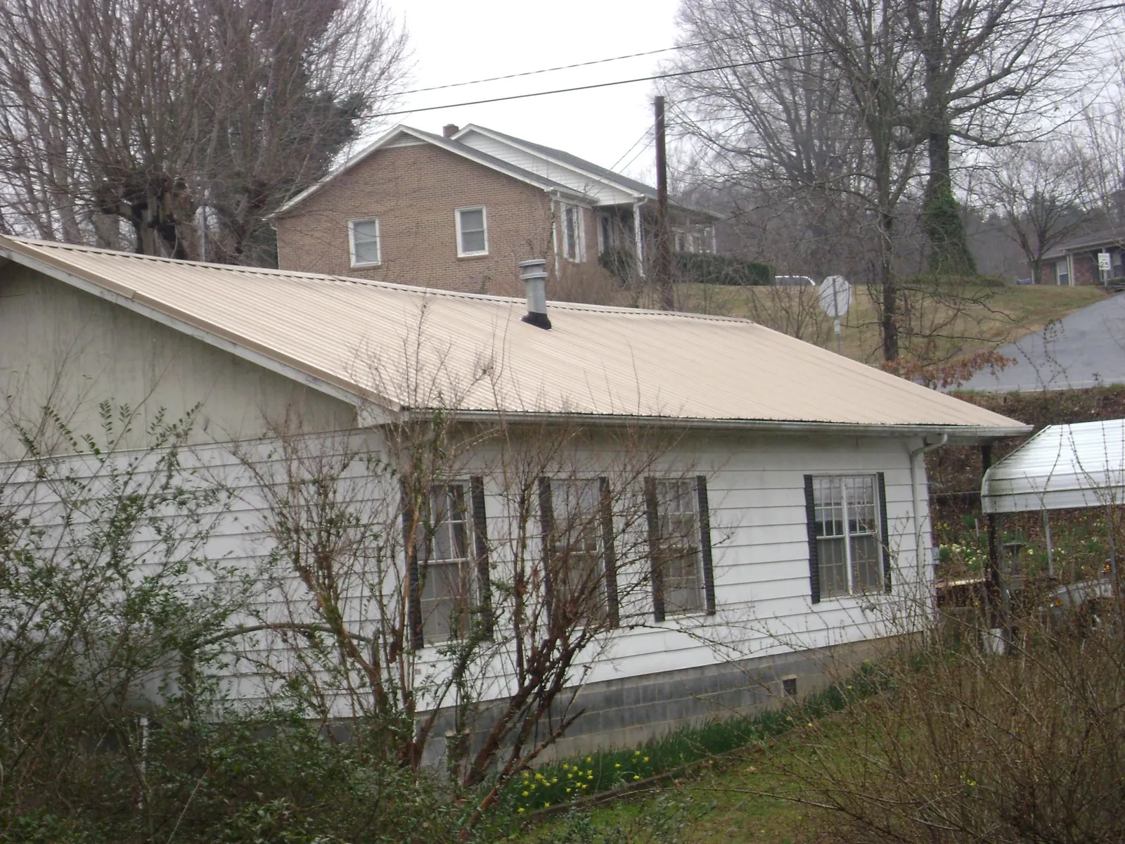 Tan metal roof on a white sided house set into a hillside — Commercial Roofing by Roofing Brothers in Stewartville